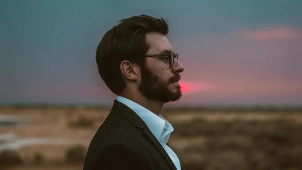 Man with glasses and beard facing to his left with sunset in the background